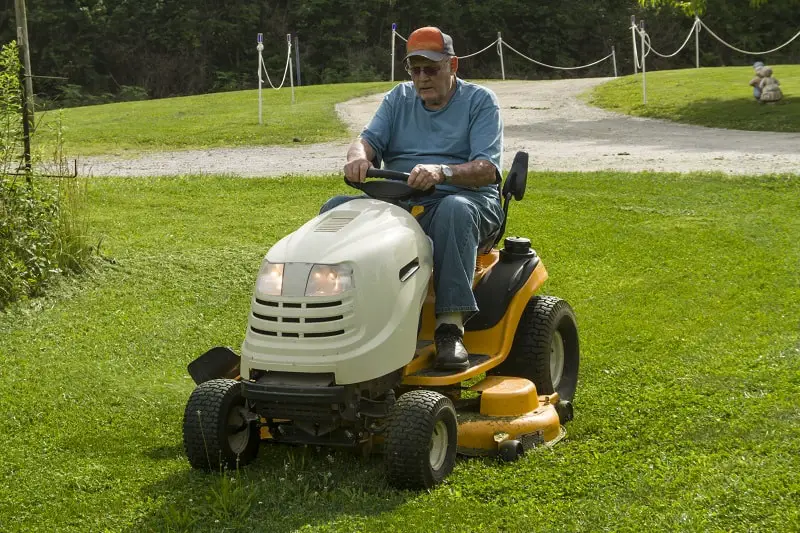 Older gentleman cutting grass on a riding lawnmower.